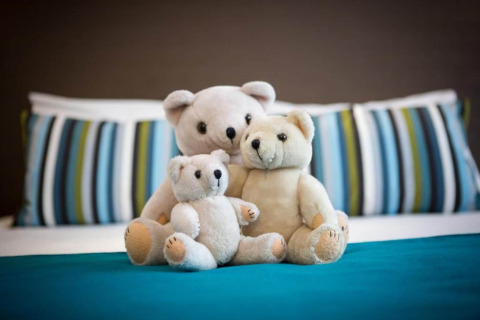 Tre orsetti di peluche seduti insieme su un letto con cuscini a righe nello chalet Het Beerenbos in Belgio.