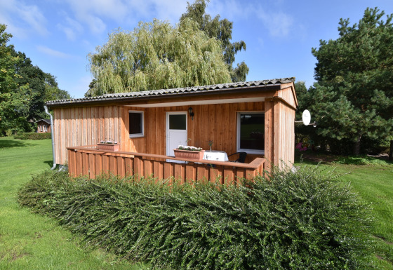 Cabaña de madera con porche y jardín, rodeada de vegetación en el complejo Gänseblümchen 2.