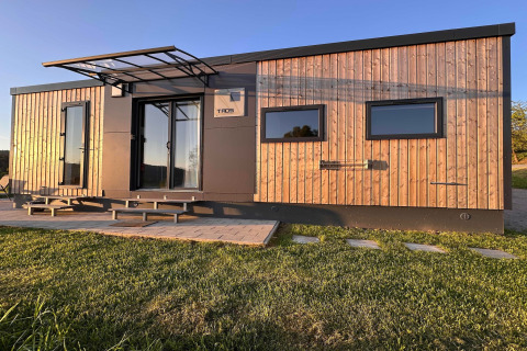 Moderne tiny house i træ og sort, Holiday village SEEBLICK, ved Eixendorfer sø under klar himmel.