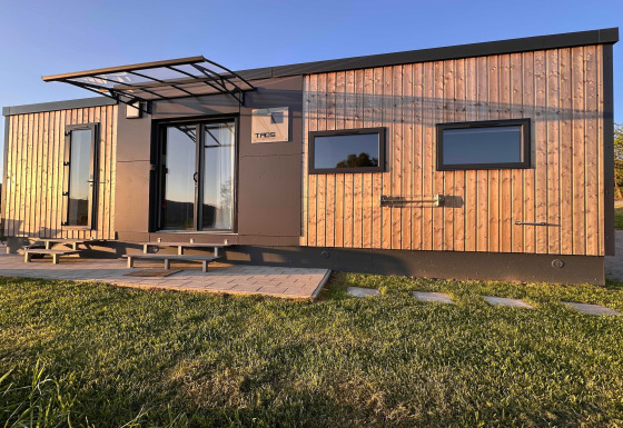 Tiny house moderna al Holiday village SEEBLICK sul lago Eixendorfer, design in legno e nero al sole.