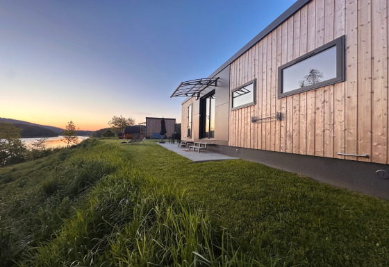 Modern tiny house by Lake Eixendorfer at sunset, featuring a patio and scenic waterfront view.