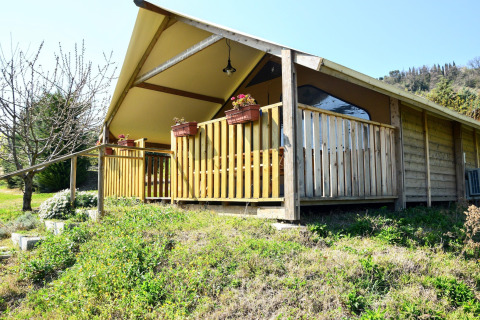 Photo of a safari tent with a wooden porch, flower boxes, and lush green surroundings.