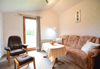 Gezellige woonkamer in de hut Platz im Grünen 2 in Duitsland met zetel, stoel en tafel bij het raam.