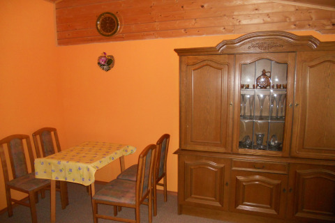 Kleine eetruimte in een chalet met oranje muren, vier stoelen, een tafel en een vitrinekast.
