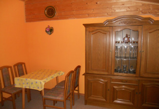 Kleine eetruimte in een chalet met oranje muren, vier stoelen, een tafel en een vitrinekast.