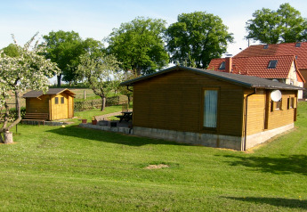 Wooden cabin 'Platz im Grünen 2' in Germany, surrounded by green grass, trees, and other houses nearby.