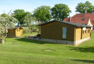 Houten vakantiewoning ‘Platz im Grünen 2’ in Duitsland, met tuin, bomen en huizen in de omgeving.