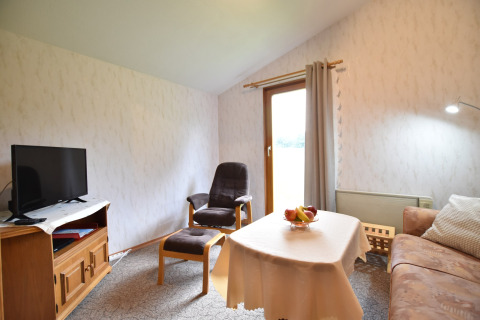 Woonkamer in de cabin Platz im Grünen 2 in Duitsland, met sofa, televisie, fauteuil en tafel met fruit.