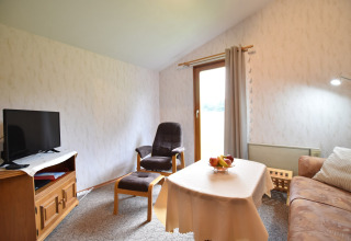 Woonkamer in de cabin Platz im Grünen 2 in Duitsland, met sofa, televisie, fauteuil en tafel met fruit.