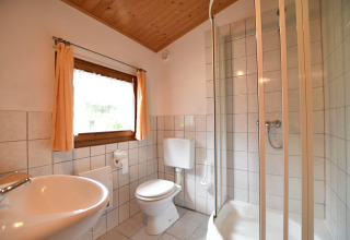 Lichte badkamer in de hut Platz im Grünen 2 in Duitsland met douche, wastafel, toilet en raam.