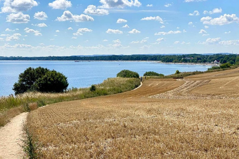 Zicht vanaf de hut Platz im Grünen 2 in Duitsland: goudkleurige akkers, water en wolkenlucht.