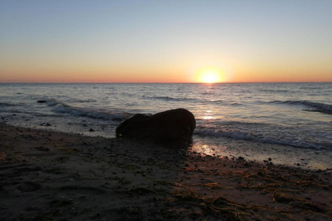 Zonsondergang boven de zee met een rots op het strand bij Platz im Grünen 2, Duitsland.