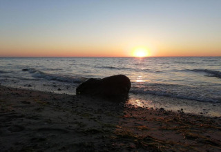 Zonsondergang boven de zee met een rots op het strand bij Platz im Grünen 2, Duitsland.