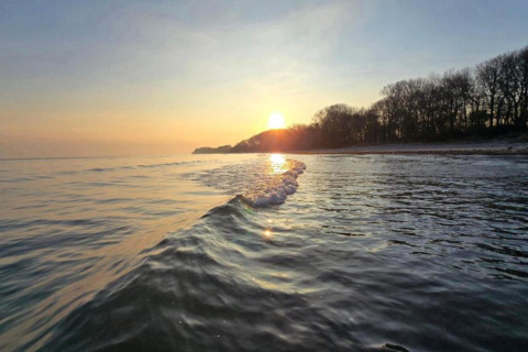 Zonsondergang boven het water aan het strand met bomen, gezien vanaf ‘Platz im Grünen 2’ in Duitsland.
