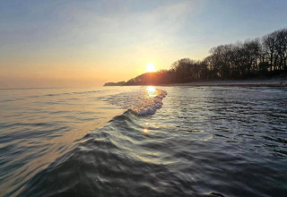 Zonsondergang boven het water aan het strand met bomen, gezien vanaf ‘Platz im Grünen 2’ in Duitsland.