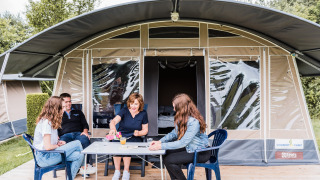 Gezin ontspant voor een safaritent op Camping Nommerlayen 1, genietend van drankjes en een spel.