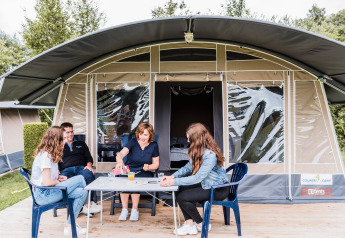 Familie hygger sig foran en safari-telt på Camping Nommerlayen 1, nyder udendørs spil og drikkevarer.