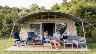 Gezin ontspant voor een safaritent bij Camping Nommerlayen 2, zittend op moderne tuinmeubels in de natuur.