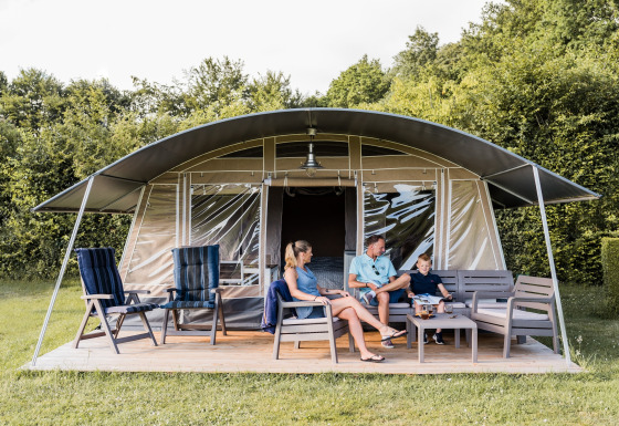 En familie slapper af foran en safari-telt på Camping Nommerlayen 2 med moderne havemøbler og natur.
