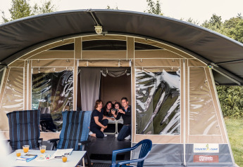 Une famille sourit et prend un selfie à l'entrée d'une tente safari, avec chaises et table à l'extérieur.