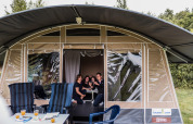 Una famiglia sorride e scatta un selfie all'ingresso di una tenda safari, con sedie e tavolo all'esterno.