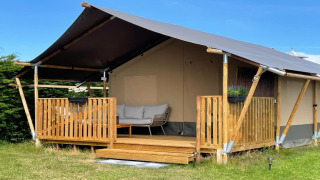 Foto di una tenda safari di lusso ad Ameland con veranda in legno, divano e area verde tranquilla.