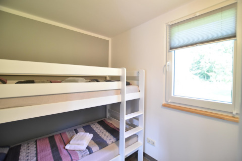 Habitación luminosa con litera y ventana, tomada en el complejo de bungalows «Gänseblümchen 2» en Alemania.