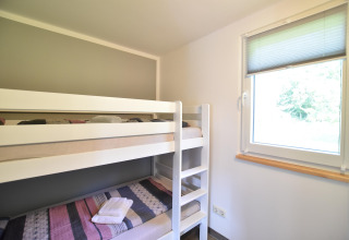 Habitación luminosa con litera y ventana, tomada en el complejo de bungalows «Gänseblümchen 2» en Alemania.