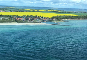 Coastal view from Bungalow complex “Gänseblümchen 2” in Germany, showing sea, beach, and yellow fields inland.