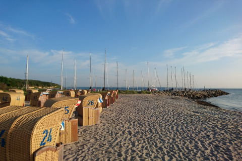 Playa con sillas de mimbre y veleros al fondo en el complejo de bungalows «Gänseblümchen 2» en Alemania.