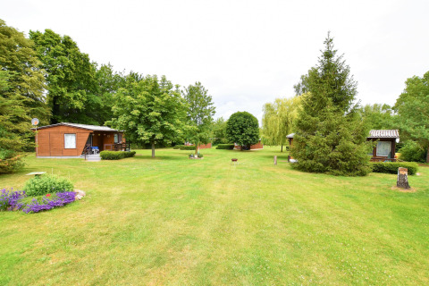 Césped verde con árboles y cabañas de madera en el complejo de bungalows «Gänseblümchen 2» en Alemania.