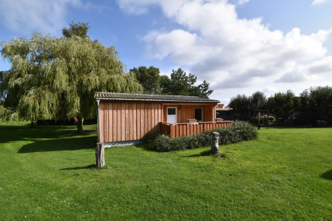 Træbungalow ved Gänseblümchen 2 i Tyskland, omgivet af grøn græsplæne og store træer under blå himmel.