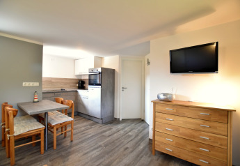 Intérieur lumineux de bungalow avec cuisine moderne, coin repas, commode en bois et télévision murale.
