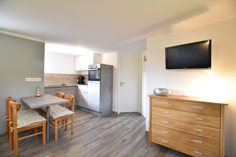 Interior luminoso de cabaña con cocina moderna, mesa de comedor, cómoda de madera y televisor en la pared.
