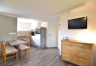 Interior luminoso de cabaña con cocina moderna, mesa de comedor, cómoda de madera y televisor en la pared.