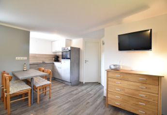Bright cabin interior with modern kitchen, small dining area, wooden dresser, and wall-mounted TV.