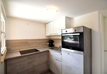 Modern kitchen in Bungalow complex “Gänseblümchen 2” in Germany with grey cabinets and built-in oven.