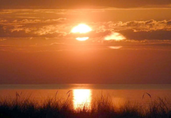 Coucher de soleil sur un lac vu d'une cabane, ciel orange-rouge, nuages et reflet du soleil dans l'eau.