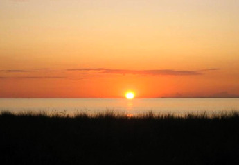 Coucher de soleil vu d'une cabine, silhouette d’herbes noires devant l’eau calme et le ciel orangé.