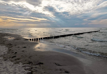 Lever de soleil sur la plage avec vagues, sable et digues au complexe Gänseblümchen 2 en Allemagne.