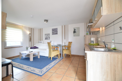 Bright living space in Bungalow complex Gänseblümchen 7, Germany, featuring kitchen, sofa, and dining area.