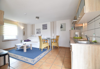 Bright living space in Bungalow complex Gänseblümchen 7, Germany, featuring kitchen, sofa, and dining area.