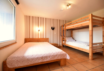 Slaapkamer in bungalowcomplex «Gänseblümchen 7» met tweepersoonsbed, stapelbed en gestreepte muur.