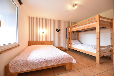 Room at bungalow complex ‘Gänseblümchen 7’ in Germany with a double bed, bunk bed, and striped wall décor.