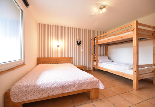 Room at bungalow complex ‘Gänseblümchen 7’ in Germany with a double bed, bunk bed, and striped wall décor.