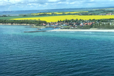 Aerial view of Bungalow complex «Gänseblümchen 7» by the sea with beach, fields, and village in Germany.
