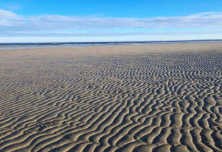 Photo de plage avec motifs ondulés sur le sable et ciel bleu, prise dans un hébergement glamping en bord de mer.