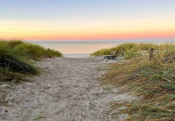 Sentier de sable avec banc et herbes de dune au coucher du soleil, pris au complexe Gänseblümchen 7 en Allemagne.