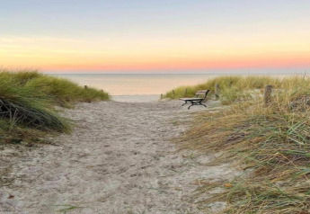 Sandy beach path with bench and dune grass at sunset, taken at Bungalow complex Gänseblümchen 7 in Germany.