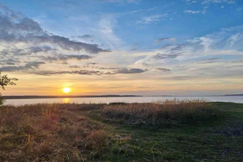 Beautiful sunset over a lake at the Bungalow complex ‘Gänseblümchen 7’ in Germany, featuring grassy shoreline.